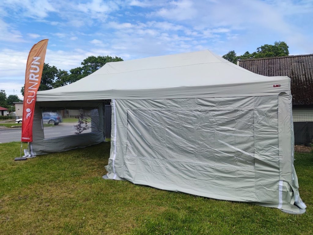 Abaja Puhkeala helehall 4 × 8 meetri suurune pop-up-telk külgseintega muruplatsil, telgi kõrval SunRuni oranž reklaamlipp.